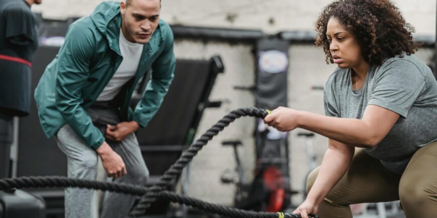 obese woman works out on the ropes with her personal trainer next to her encouraging her