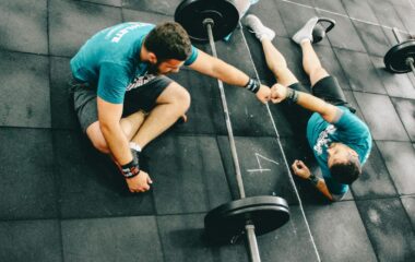 two men relaxing on the gym floor tired after strength training fist bump each other