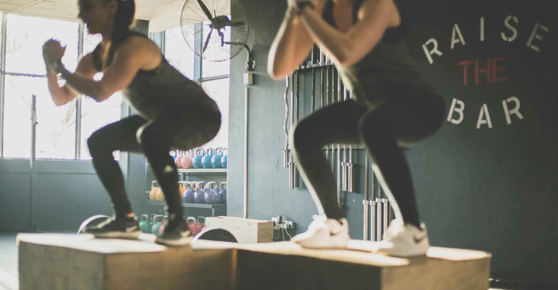 photo of two bootcamp class members jumping onto blocks and doing a squat